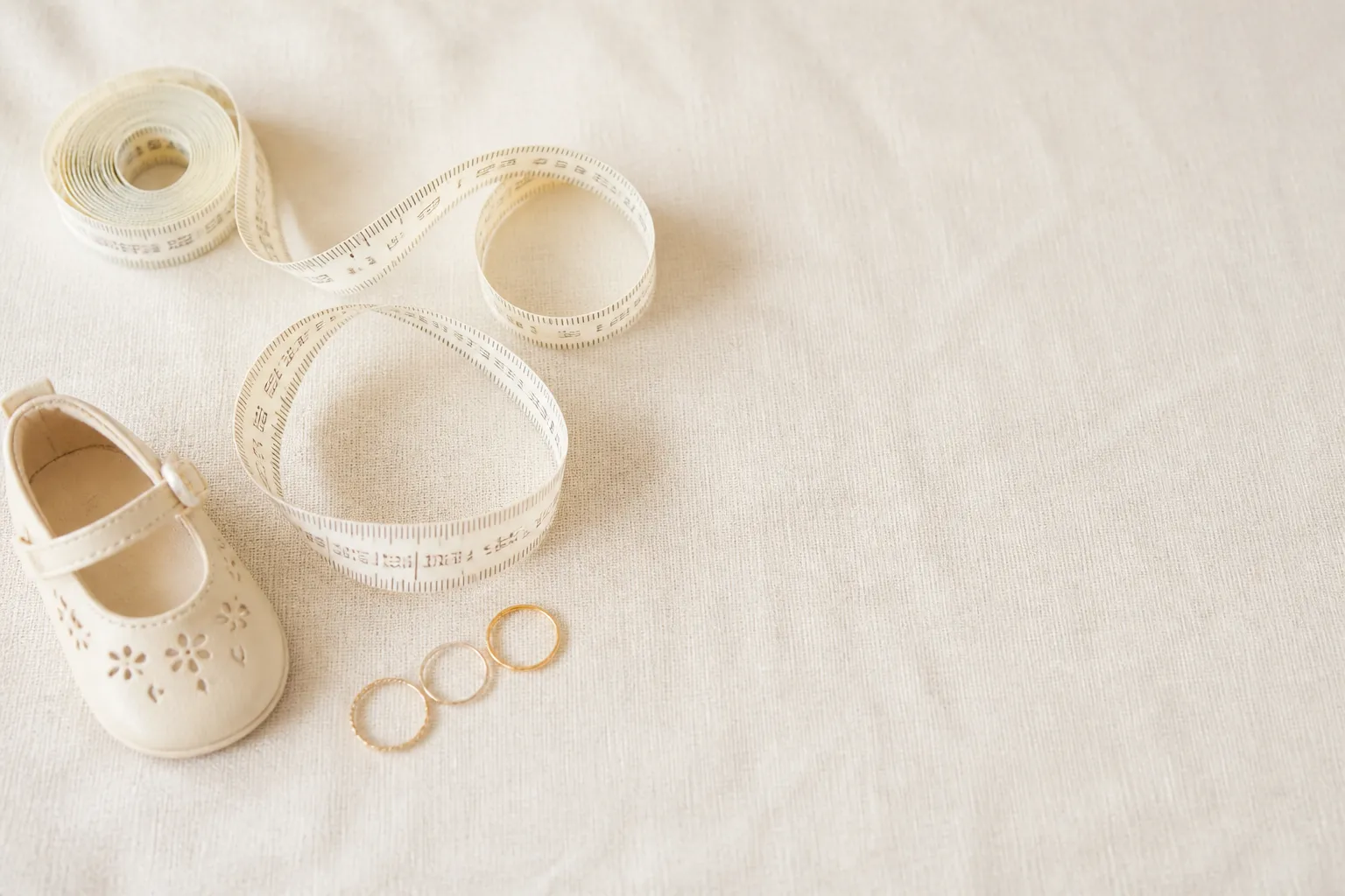 Ein Maßband, ein kleiner Schuh und drei Ringe auf hellem Leinen — Größenumrechnung leicht gemacht